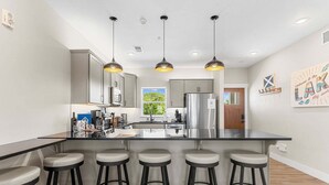 Une cuisine moderne dotée d’un îlot central, de tabourets de bar, de luminaires suspendus et d’appareils électroménagers en acier inoxydable.