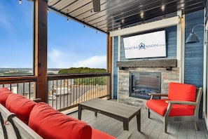 A covered outdoor seating area with a fireplace, a sign for RENTBRNSON.COM, and a view of the landscape. - Ultimate Game Room Retreat w Putting Green_Great Lake Views_Free Tickets & Community In/Outdoor Pool (Branson)