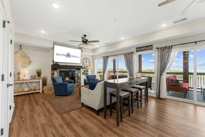 A spacious living area with a fireplace, a ceiling fan, and a large TV screen.