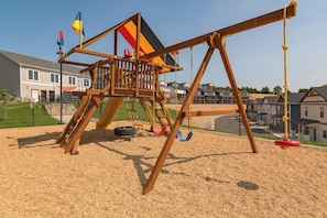 A playground with a wooden swing set and a climbing structure, surrounded by a fence and houses in the background. - Near Silver Dollar City with Private Hot Tub, Game Area, Community Indoor Pool & Free Daily Tickets (Branson)