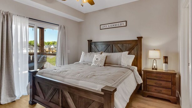 A bedroom with a wooden bed, a nightstand, a ceiling fan, and a view of a balcony.