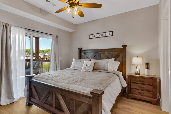 A bedroom with a wooden bed, a nightstand, a ceiling fan, and a view of a balcony.