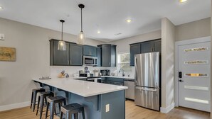 A modern kitchen with dark cabinets, a large island, stainless steel appliances, and pendant lighting.