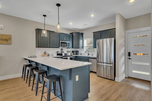 A modern kitchen with dark cabinets, a large island, stainless steel appliances, and pendant lighting.