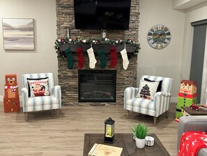 A cozy living room with a fireplace, two armchairs, a coffee table with a lantern, and festive decorations. - Near Silver Dollar City with Private Hot Tub, Game Area, Community Indoor Pool & Free Daily Tickets (Branson)