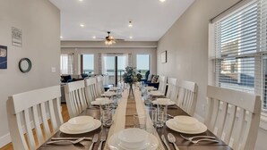 A dining room with a long table set for six, white chairs, and a ceiling fan.