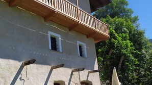 Un bâtiment de style rustique doté d’un balcon, d’un petit jardin fleuri et d’un espace extérieur aménagé pour s’asseoir.