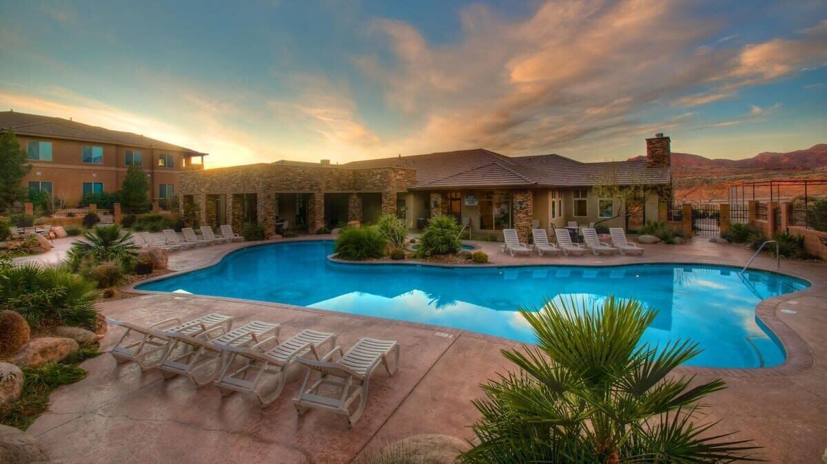 A swimming pool with lounge chairs, a stone building, and a desert landscape in the background.