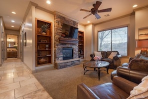 A living room with a stone fireplace, leather furniture, and a ceiling fan. - Ground Floor Suite | Private Balcony, Poolside Access (Hurricane)