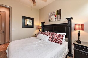 A neatly arranged bedroom with a large bed, a headboard, two bedside lamps, a framed mirror, and a painting on the wall.