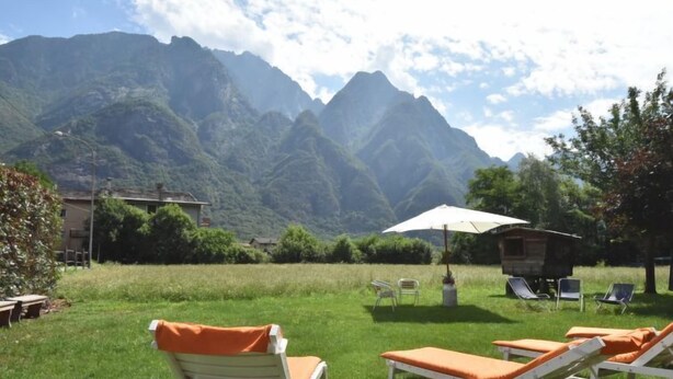 Un espace verdoyant avec des chaises longues et un parasol, le tout situé devant un paysage de montagnes.