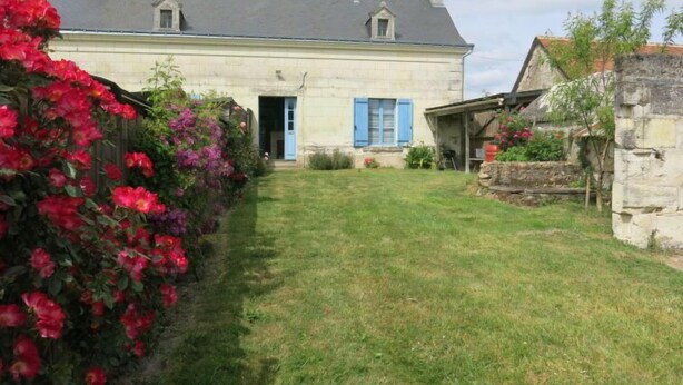Una casa de dos pisos con puerta principal, un pequeño porche y un jardín con flores rojas.