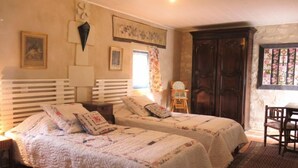 Un dormitorio con dos camas, un armario de madera, una silla y una ventana con cortinas florales.