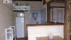 Cocina compacta con un refrigerador blanco, un microondas y un mueble de madera con una pequeña mesa.