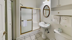 Un bagno con cabina doccia in vetro, lavandino su piedistallo, water e specchio.