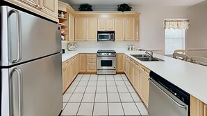 Una cucina con mobili chiari in legno, un frigorifero in acciaio inossidabile, un forno a microonde, un forno e una lavastoviglie.