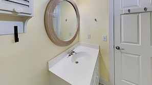 Une salle de bain avec un lavabo blanc, un miroir rond et une porte blanche.