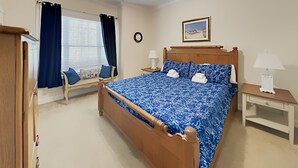 A bedroom with a wooden bed, a bench with cushions, a bedside table with a lamp, and a wall clock. - Tranquil Hideaway 4 Bdrm Condo in Avian Forest (Pawleys Island)