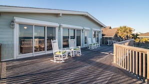 A covered deck with white rocking chairs and a wooden railing.