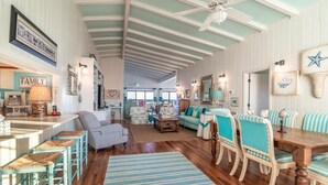 A spacious living room with a high ceiling, wooden floors, and a dining area with striped chairs.