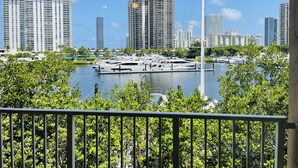 A marina with yachts docked, surrounded by high-rise buildings and lush greenery.