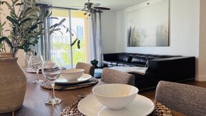 A dining area with a table set for two, a black leather sofa, and a ceiling fan.
