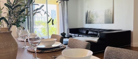 A dining area with a table set for two, a black leather sofa, and a ceiling fan.