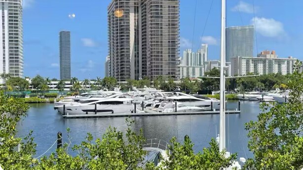 A marina with several yachts docked, surrounded by high-rise buildings and greenery.