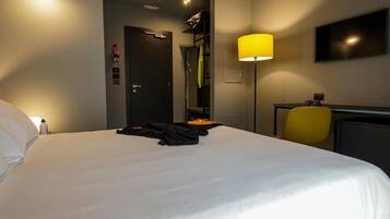 A hotel room with a large bed, a desk with a chair, a TV on the wall, and a door leading to a bathroom.