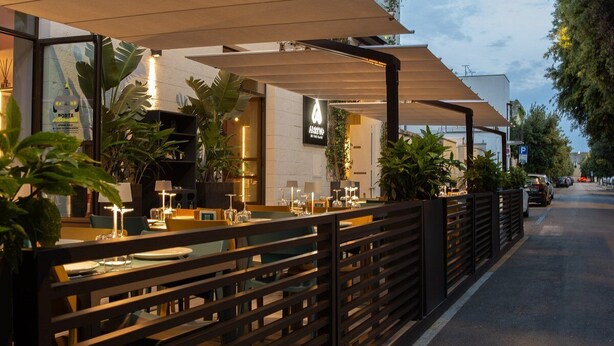 An outdoor cafe with tables and chairs, a wooden fence, and umbrellas providing shade. - Arryvo (Lecce)