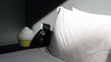 A bed with white pillows and a cupcake on a bedside table.