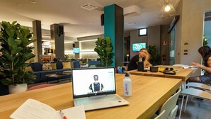 A modern hotel lobby with a seating area, a reception desk, and a large screen displaying a video call. - Arryvo (Lecce)
