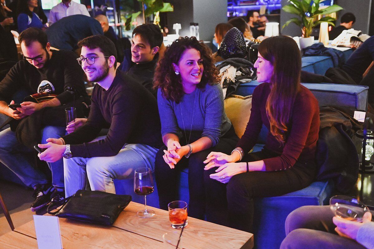 Um grupo de pessoas sentadas em sofás numa área de estar, com uma mesa em primeiro plano.