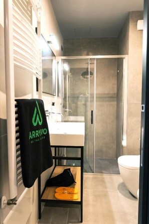 A modern bathroom with a glass shower enclosure, a white sink, and a towel rack with a logo.