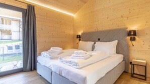 A modern bedroom with a large bed, two bedside lamps, and a view of the outdoors through a large window. - Premium mit 4 Schlafzimmern,Sauna&Pool by Interhome (Haus)