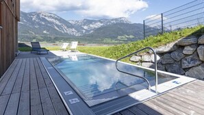 A swimming pool with two lounge chairs, a wooden deck, and a mountain view. - Premium mit 4 Schlafzimmern,Sauna&Pool by Interhome (Haus)