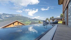 An infinity pool with a mountain view, wooden deck, and lounge chairs.