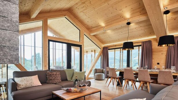 A spacious living area with a wooden ceiling, large windows, and a dining area with chairs and a table.