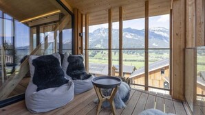 A wooden deck with two bean bags and a small table, overlooking a mountainous landscape.