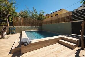 Une piscine rectangulaire dotée d’une terrasse en bois et d’un escalier menant à l’eau, le tout entouré d’une clôture en bambou et d’arbres.
