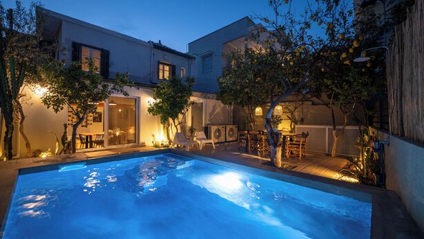 Une piscine avec un espace patio, du mobilier d’extérieur et un bâtiment doté d’une porte et de fenêtres.