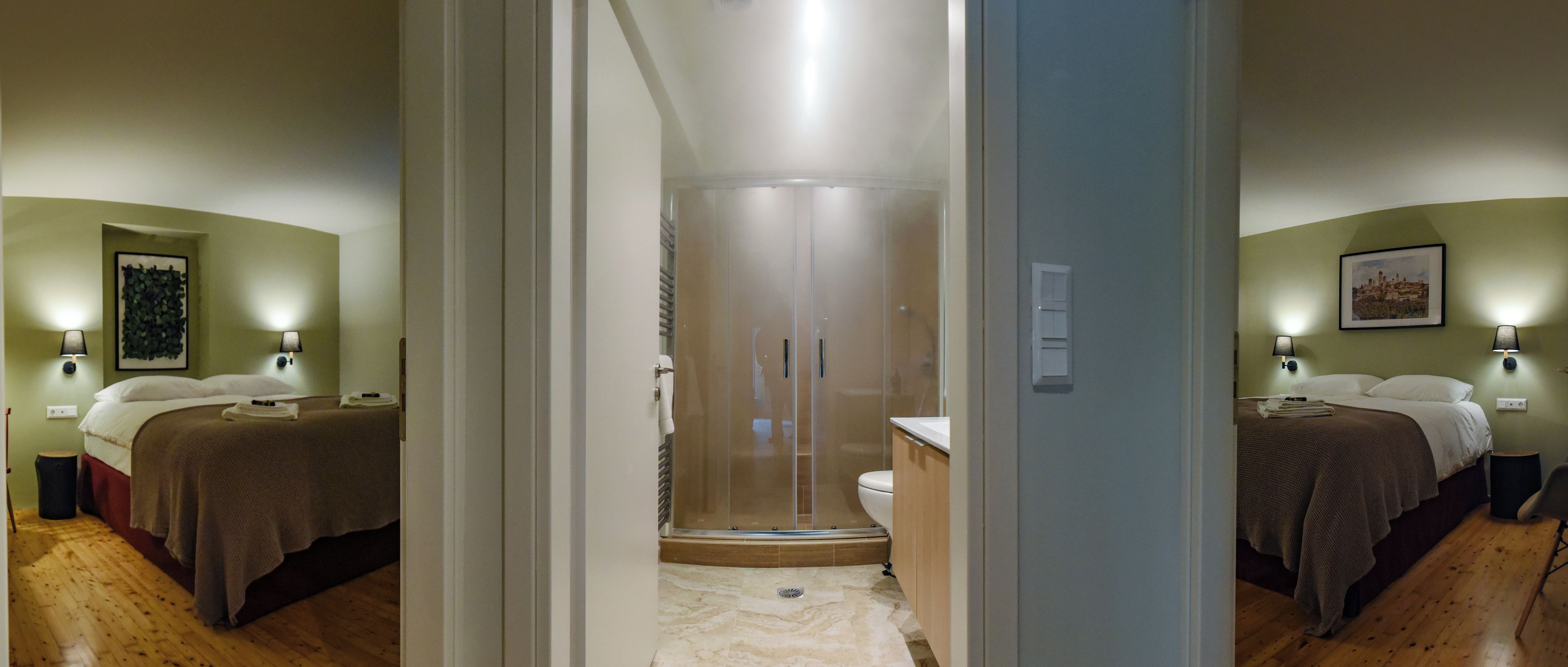 A hotel room with a bed, bedside table, and a shower area with a glass door.