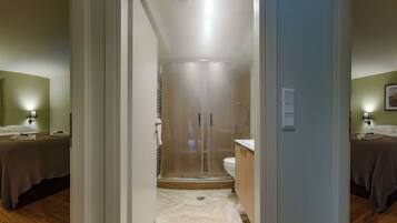A hotel room with a bed, bedside table, and a shower area with a glass door.