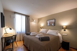 Une chambre d’hôtel avec un lit, un bureau, une chaise et une fenêtre avec des rideaux.
