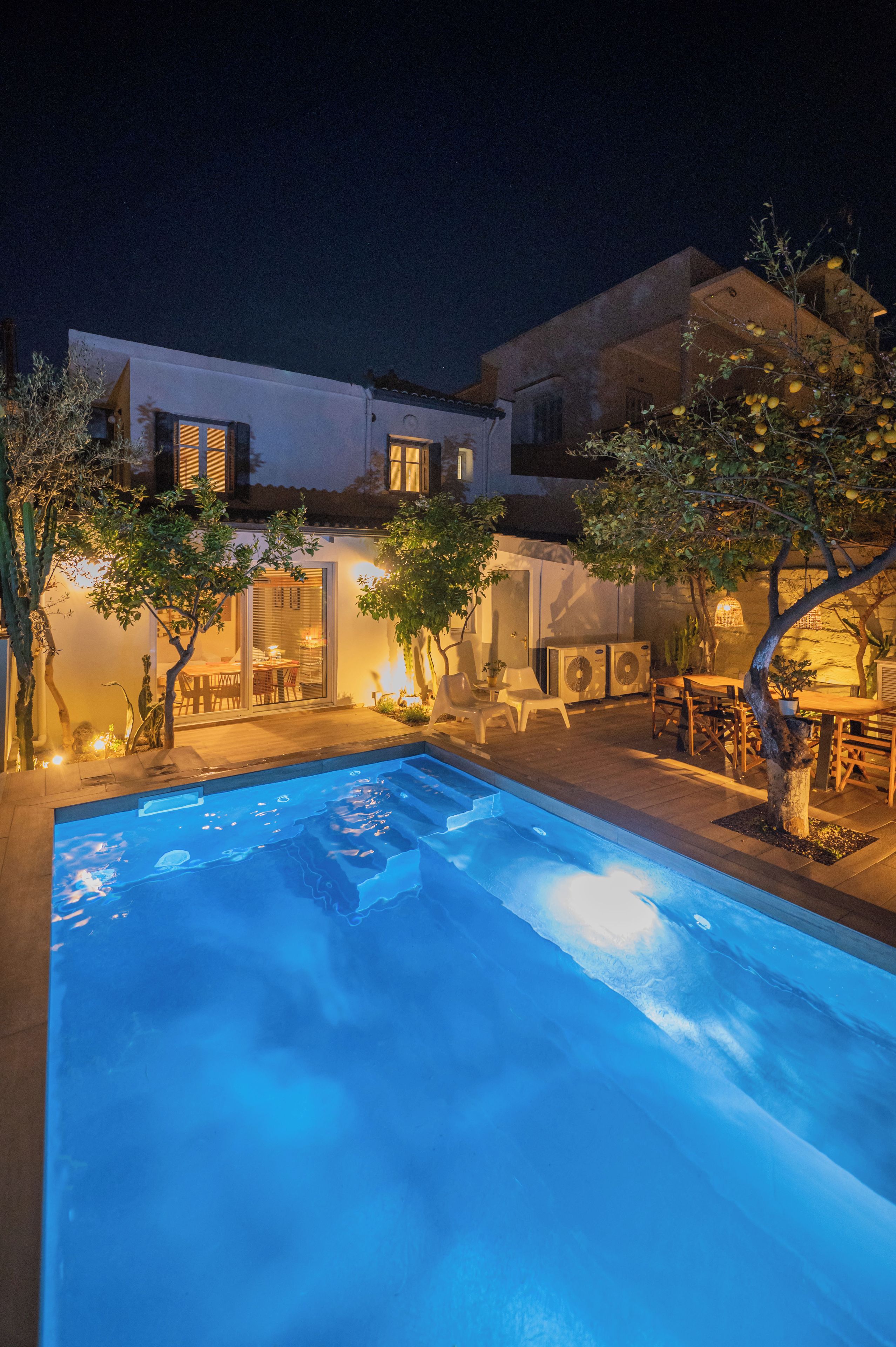 Ein Swimmingpool mit Terrassenbereich, Gartenmöbeln und einem Gebäude mit mehreren Fenstern und Balkonen.