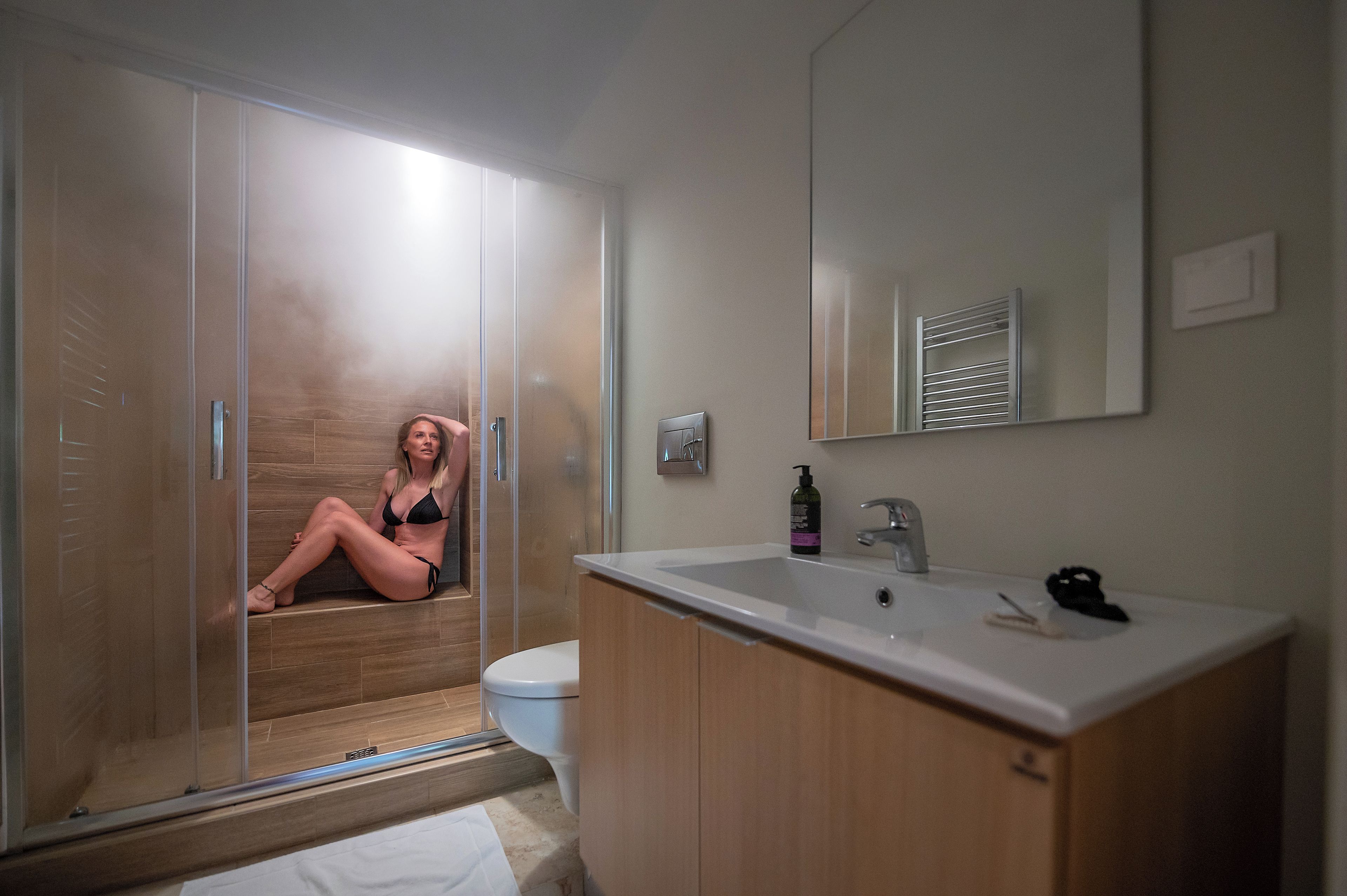 Ein Badezimmer mit Duschkabine aus Glas, einem weißen Waschbecken und einem Spiegel darüber.