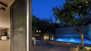 A modern outdoor pool area with a wooden deck, a seating area with chairs, and a dining table.