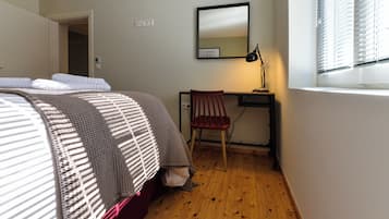 Ein Schlafzimmer mit Bett, Schreibtisch, Stuhl, Spiegel und einem Fenster mit Jalousien.