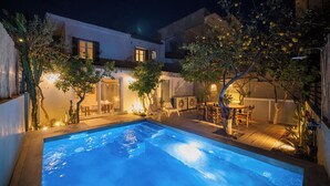Une piscine avec un espace patio, du mobilier d’extérieur et un bâtiment doté de nombreuses fenêtres et portes.