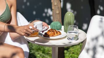 Eine Frau sitzt an einem Tisch im Freien mit einem Teller Essen, einem Glas Wasser und einer Kakteendekoration.